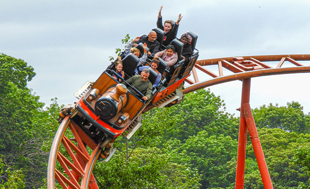 People on a rollercoaster train with trees and sky in the background