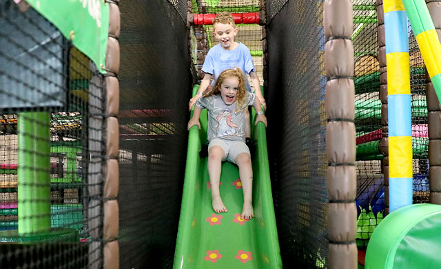 Young boy and young girl on a slide in a soft play area